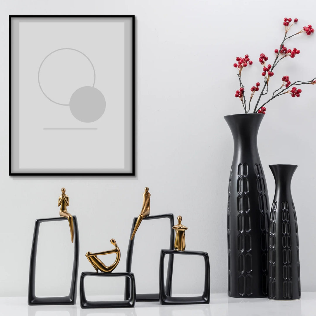 Decorative items including black vases and sculptures on a white surface with a framed abstract art piece.