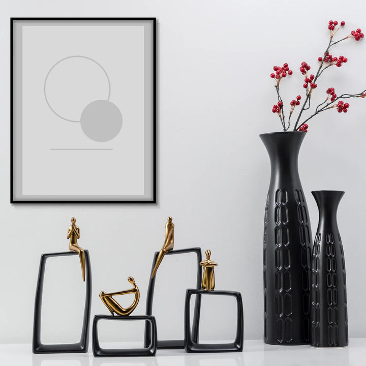 Decorative items including black vases and sculptures on a white surface with a framed abstract art piece.