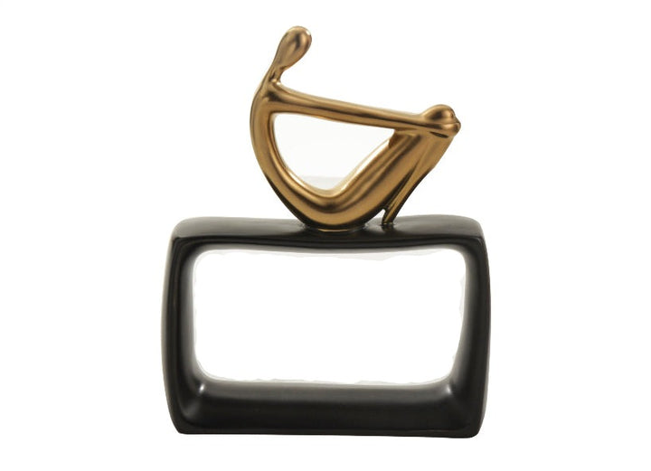 A high-quality ceramic sculpture featuring an abstract human figure in gold sitting on a black rectangular base.