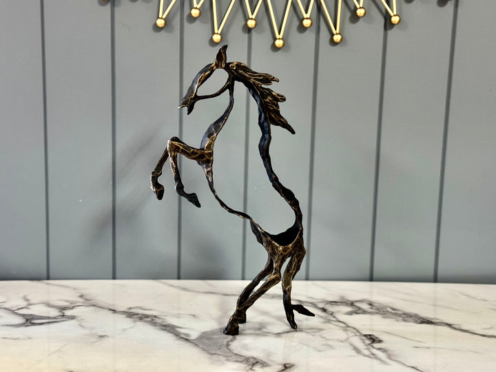 A bronze-colored abstract rearing horse sculpture with an open-frame design, placed on a marble surface.