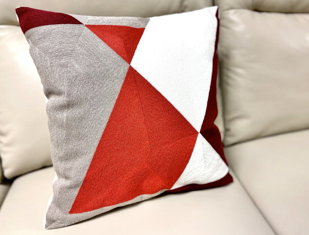 A square-shaped cushion with a geometric pattern featuring red, white, and gray colors, with a zip closure.
