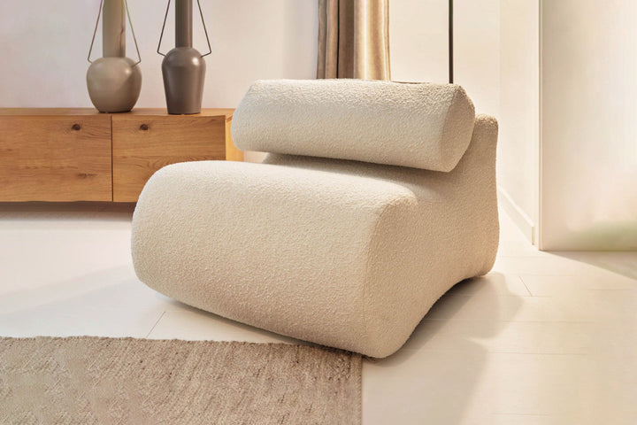 Beige armchair in a modern living room setting with wooden cabinet and decorative vases.