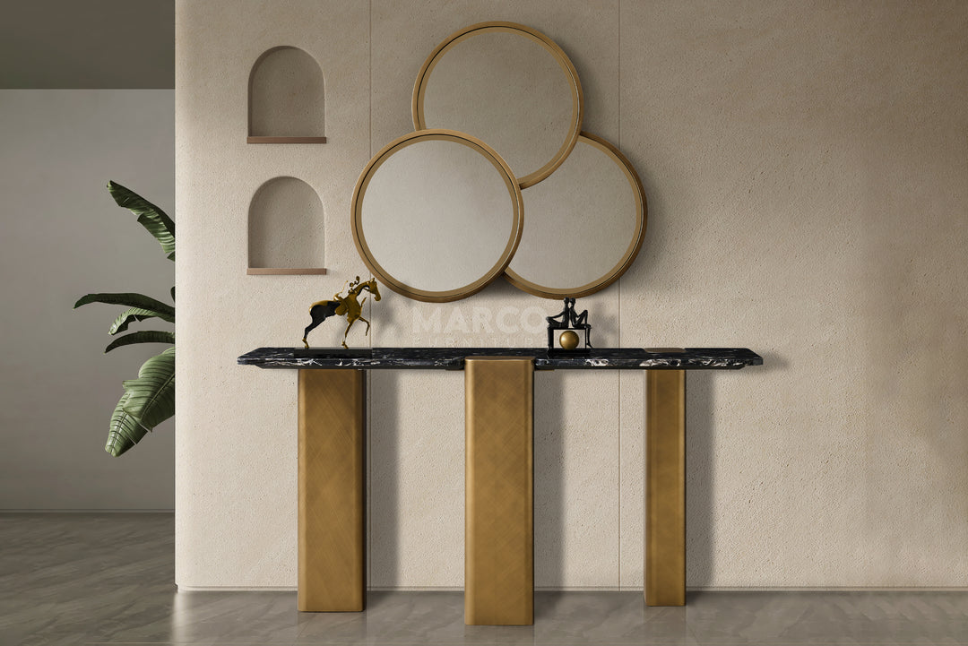 Decorative console table with gold legs and black marble top against a beige wall with circular mirrors.