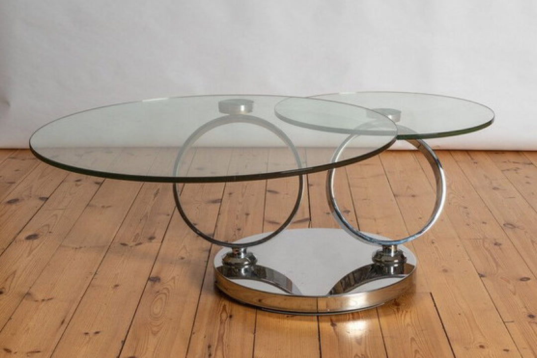Glass coffee table with metal circular base on wooden floor.