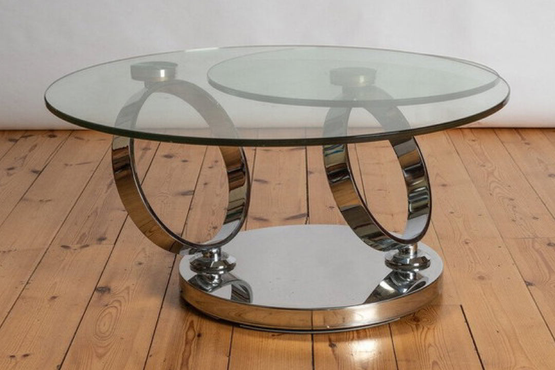 Glass coffee table with chrome circular base on wooden floor.