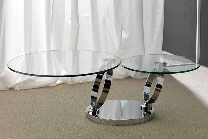 Glass coffee table with chrome ring base in front of white curtains.