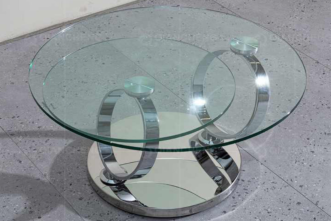 Glass coffee table with chrome metal base on a concrete floor.
