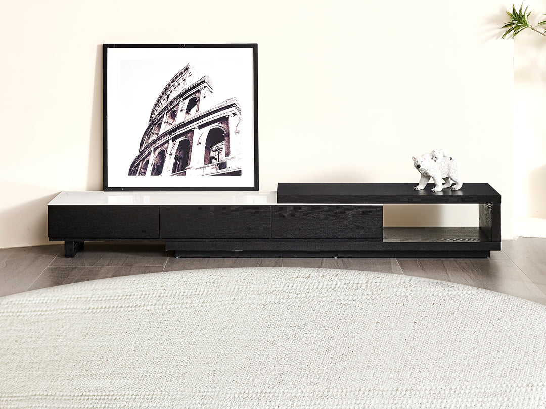 A modern extendable entertainment unit with a black oak veneer structure and a white sintered stone top, featuring a framed artwork and decorative items on it, placed above a white rug.