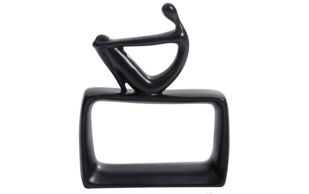 A black ceramic abstract thinking man figurine sitting on a hollow rectangular base.