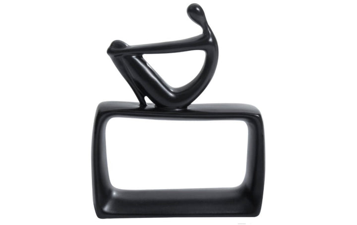A black ceramic abstract thinking man figurine sitting on a hollow rectangular base.