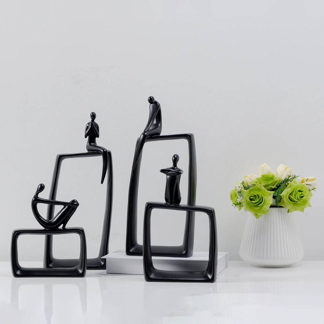 Set of black abstract sculptures on a white surface with a vase of green flowers.