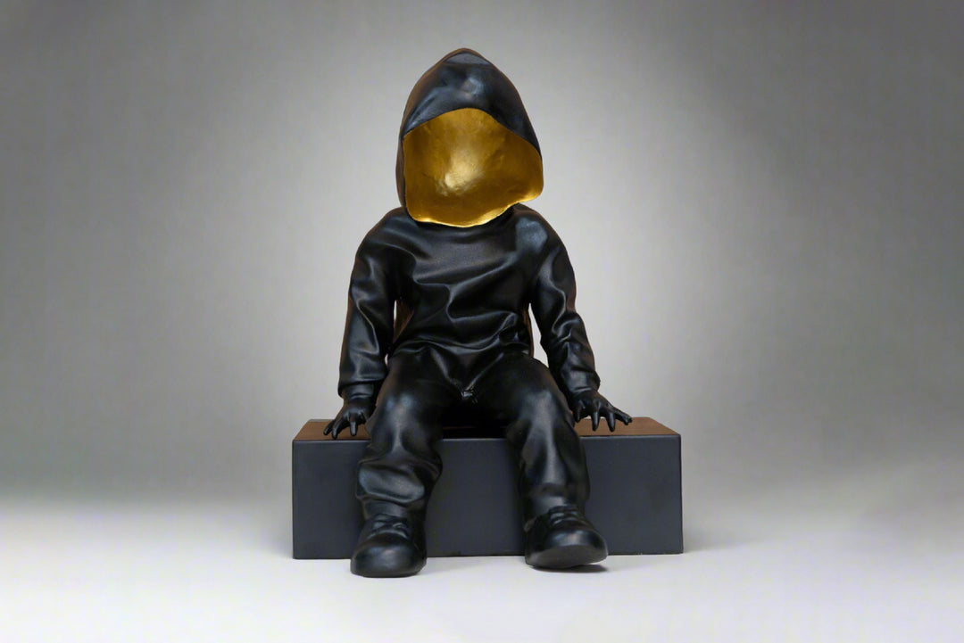 Statue of a child in a black hooded outfit with a gold head on a gray background