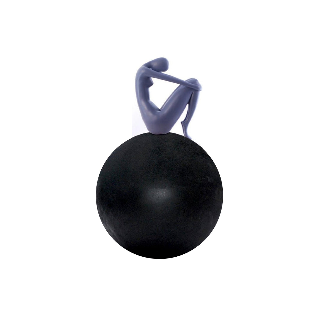 A sculpture of a human figurine sitting on a large, smooth spherical object, primarily in black color with a touch of blue.