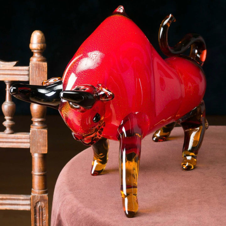 Red and amber glass bull figurine on a wooden surface with a dark background