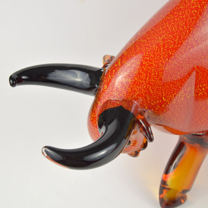 Glass sculpture of a bull with orange and black colors on a white background