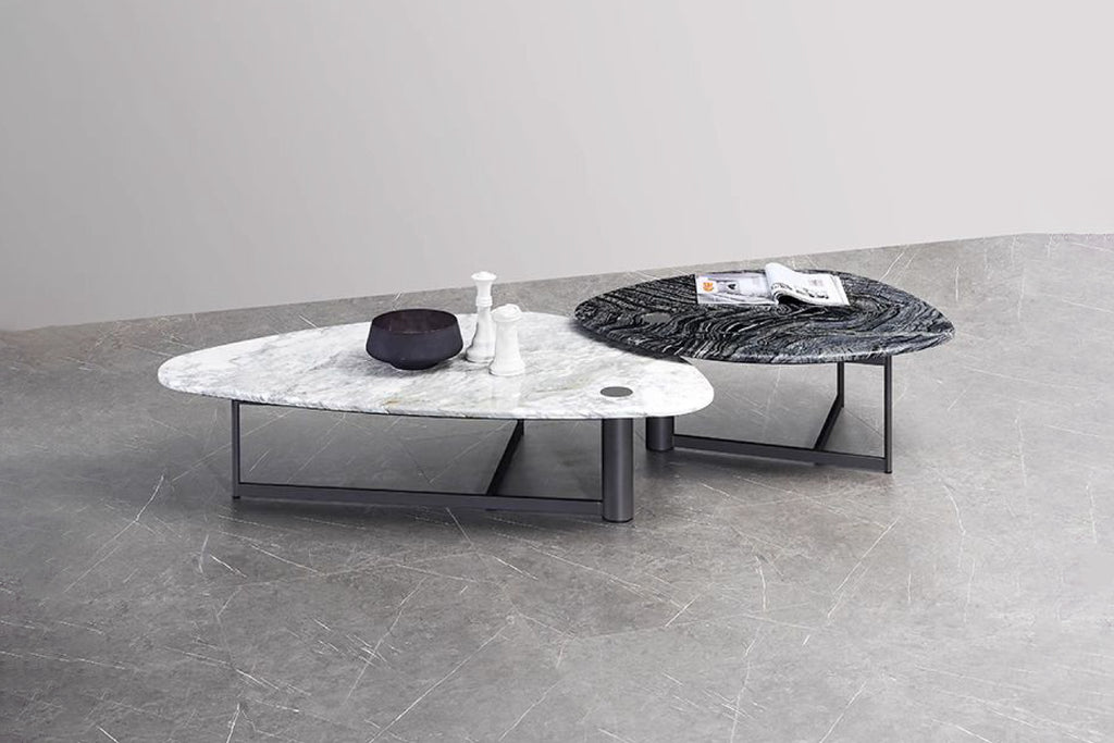 Two nesting coffee tables with a black marble top and a white marble top, respectively, both with black metallic bases, placed on a grey floor.