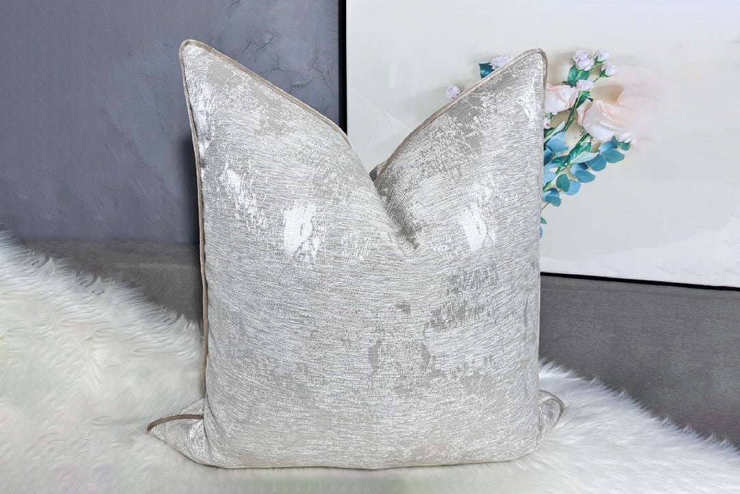 Silver textured pillow on a white surface with a blurred background