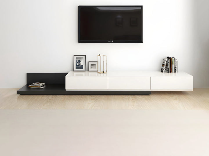 A modern TV unit with a retractable sliding top, featuring a black oak veneer base and white matte finish. It has three drawers and is positioned on a light wooden floor against a white wall, with a flat-screen TV on top.