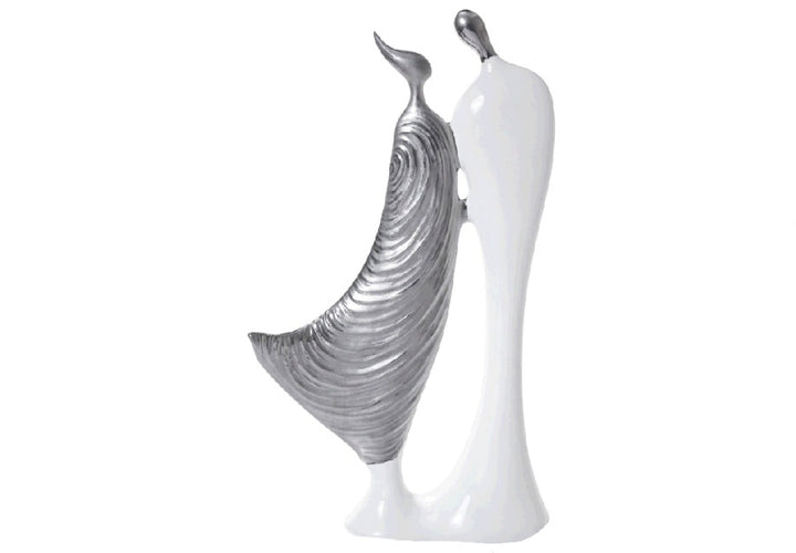 A pair of contemporary ceramic figurines of abstract human-like figures, one in glossy white and the other in textured silver/gold, placed on a white surface.