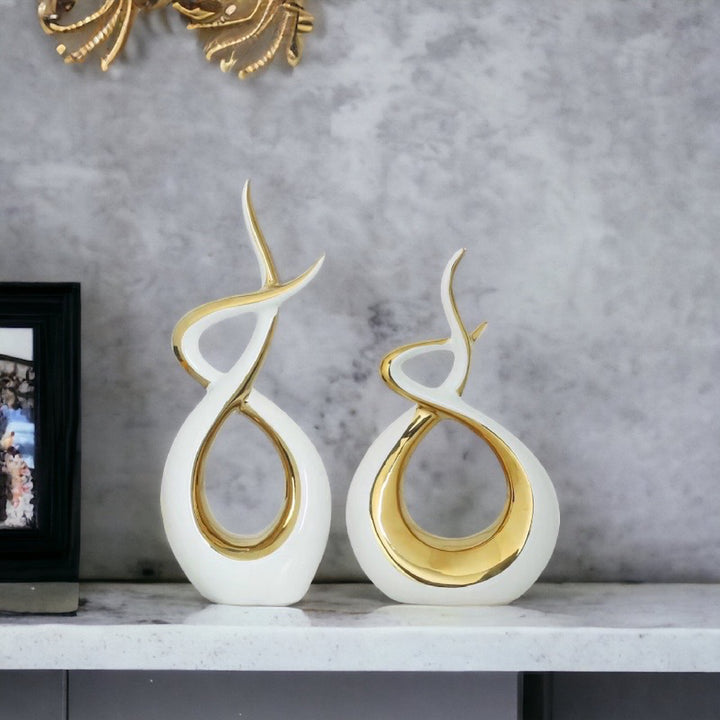 Two ceramic vases with a flame-like design, one larger than the other, finished in white with gold polish, placed on a marble surface.