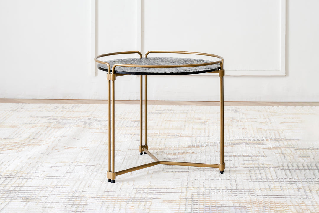 A contemporary end table with a grey ripple glass top and a metal base finished in gold.