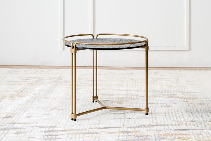 A contemporary end table with a grey ripple glass top and a metal base finished in gold.