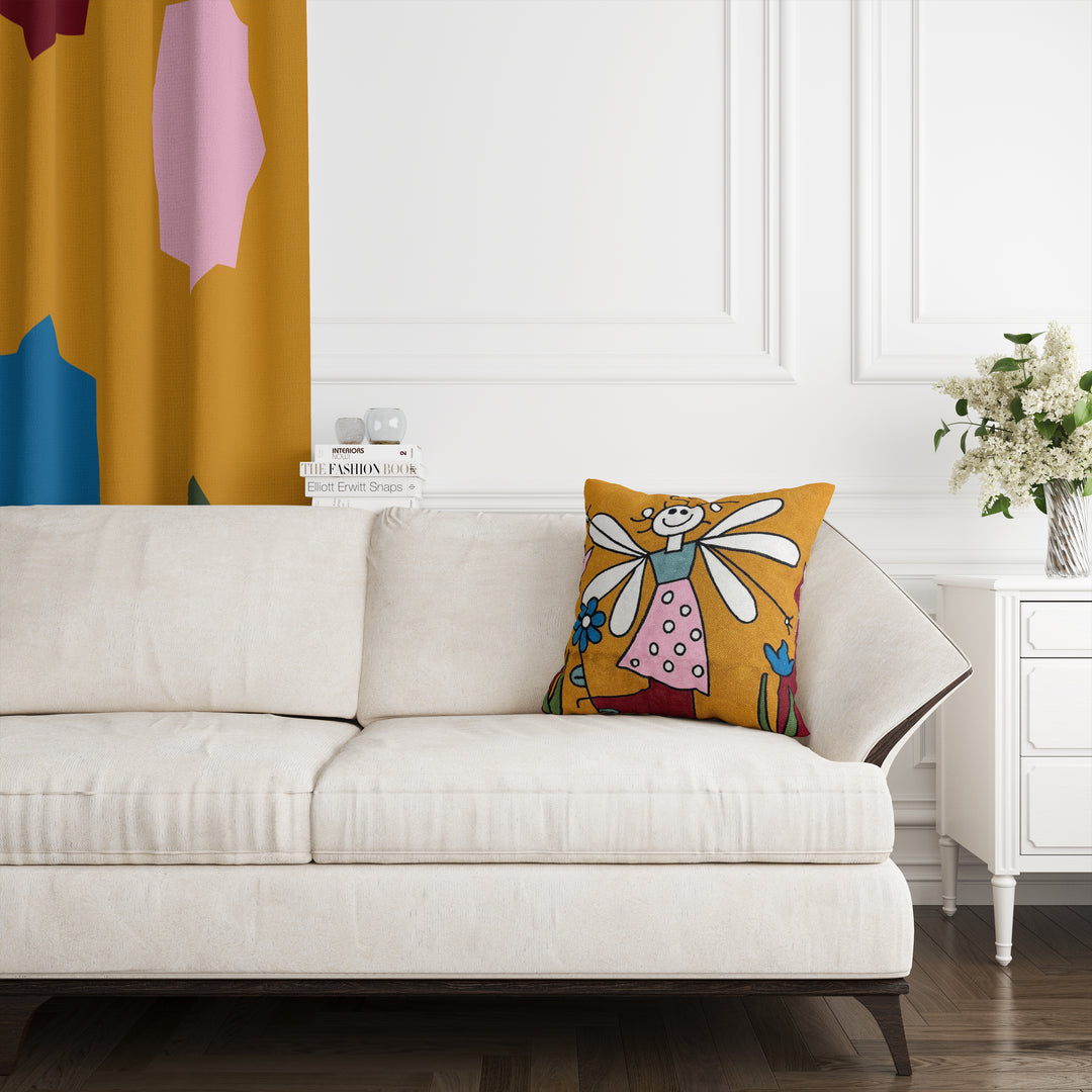 A cushion cover featuring a colorful design with a character resembling Tinker Bell on a sofa in a room with a white wall and a decorative yellow curtain.