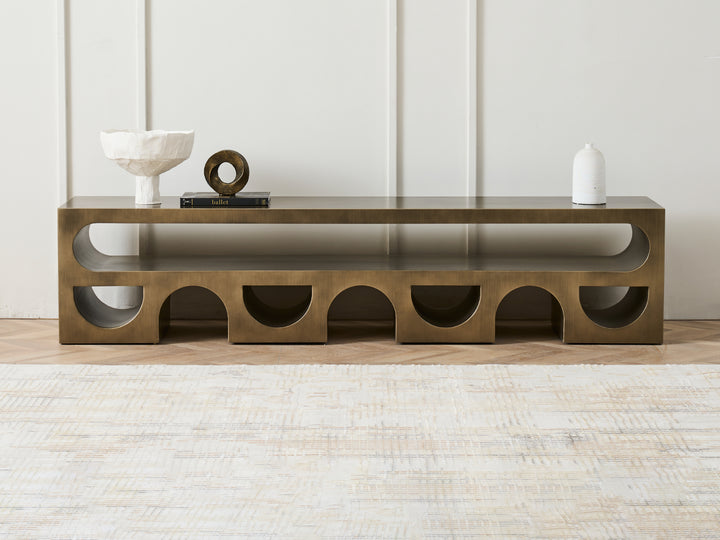 A modern gold-colored metal TV stand with an arched structure, featuring decorative items on top, placed in a contemporary room setting.