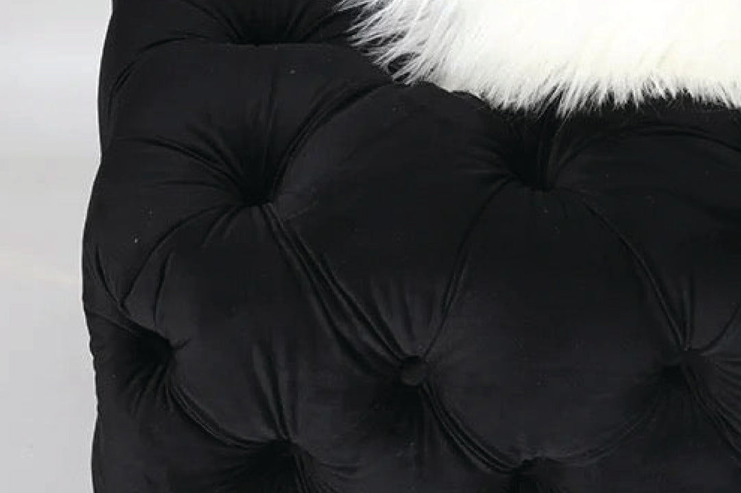 Close-up of a black tufted cushion with white fur trim on a light background