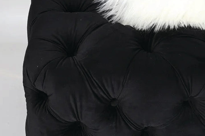 Close-up of a black tufted cushion with white fur trim on a light background