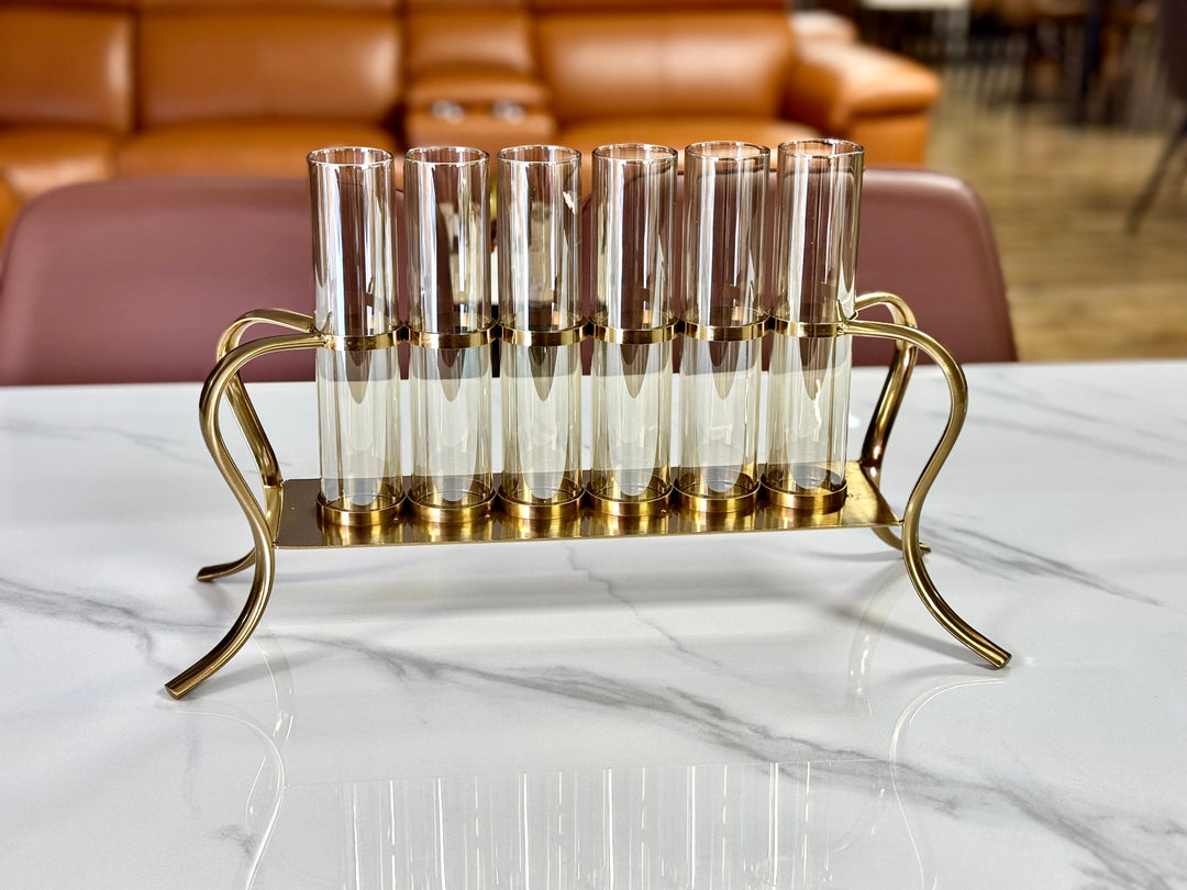 A gold multi-tube candle holder with clear glass tubes arranged in a triangular formation on a polished gold metal frame, displayed on a white surface.