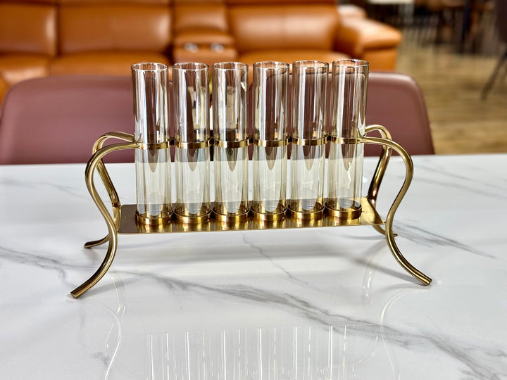 A gold multi-tube candle holder with clear glass tubes arranged in a triangular formation on a polished gold metal frame, displayed on a white surface.