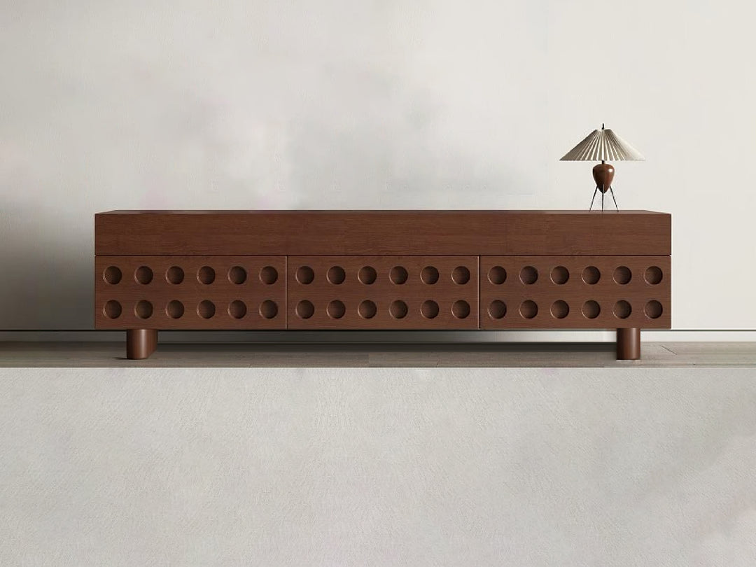 A modern TV cabinet with storage, featuring a unique circular cut-out design on the drawers, with a walnut finish and timber wood legs. A lamp is placed on top of the cabinet.