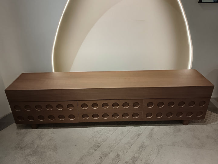 Wooden bench with circular cutouts against a plain wall.