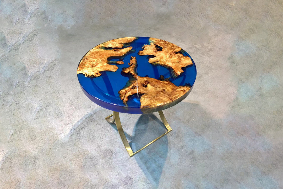 A round Live Edge Epoxy Resin Coffee Table with blue resin and gold-finished metal legs on a patterned floor.