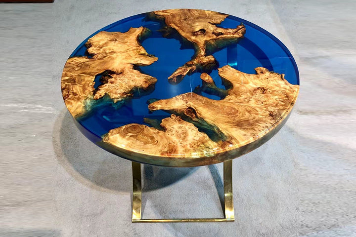A round Live Edge Epoxy Resin Coffee Table with blue resin and gold-finished metal legs on a patterned floor.