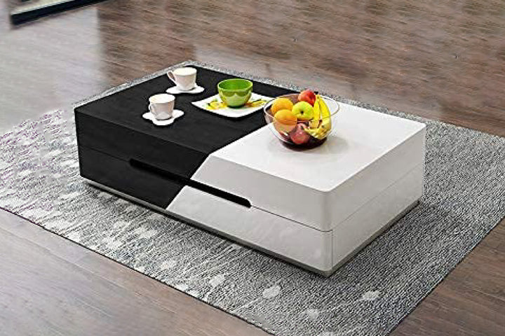 A modern coffee table with a black and white sliding top, featuring built-in storage compartments, placed on a grey area rug with a bowl of fruits and a cup on top.