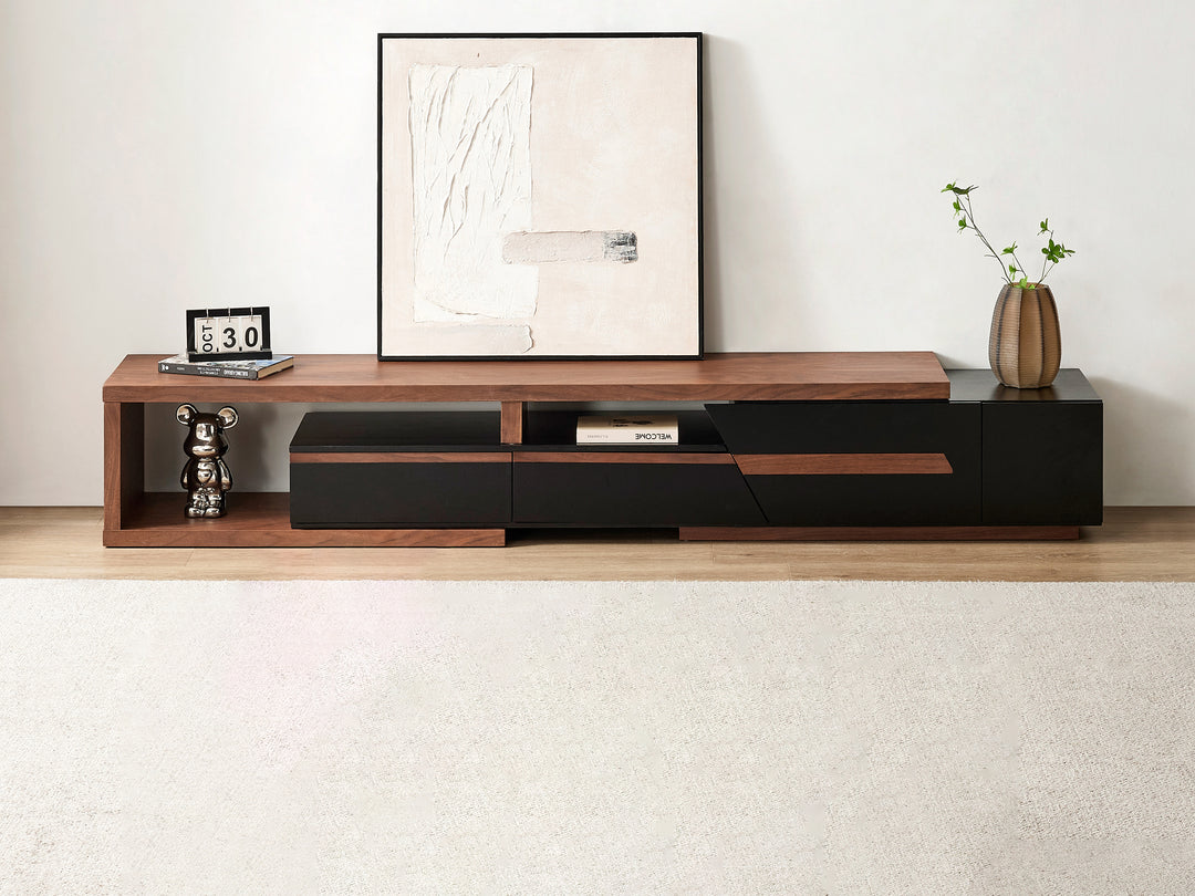 A modern TV unit with storage in walnut and black colors, featuring three drawers and an open shelf, with a framed picture, a decorative plant, and a clock on top.