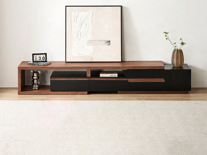 A modern TV unit with storage in walnut and black colors, featuring three drawers and an open shelf, with a framed picture, a decorative plant, and a clock on top.