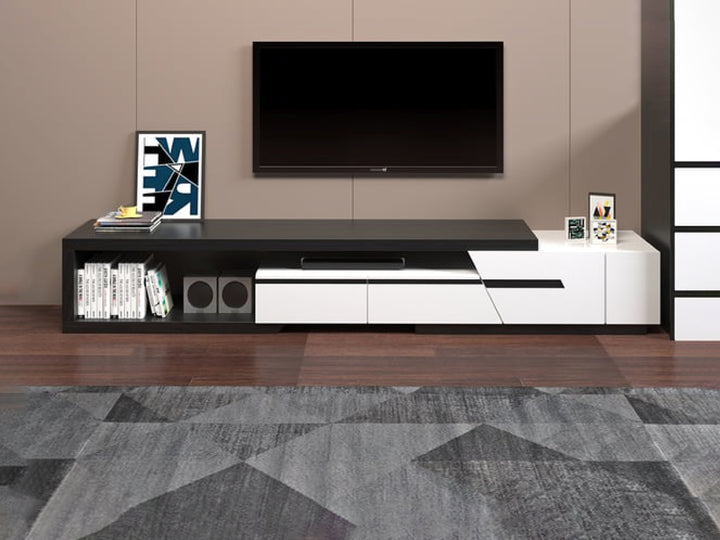 A modern TV unit with extendable functionality, featuring three large drawers and an open shelf. The unit is painted in high-gloss white with black oak veneer accents, and is displayed in a living room setting with a TV on top and decorative items.