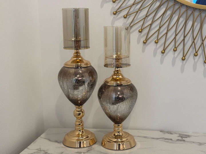 A set of two gold and glass candle holders with a glossy finish on a marble surface.