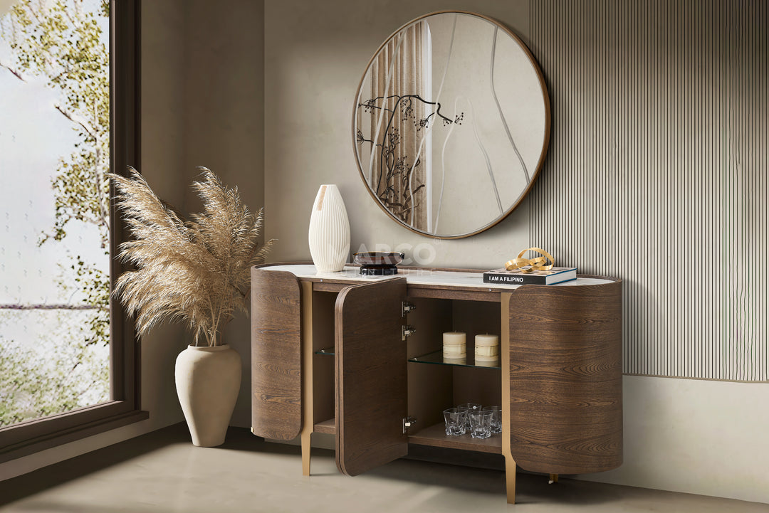 Wooden sideboard with round mirror and decorative items in a room with a window and plant.