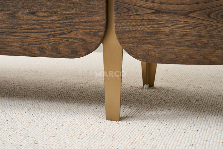 Close-up of a wooden chair leg with gold finish on a beige carpet, featuring the brand 'Marco'.