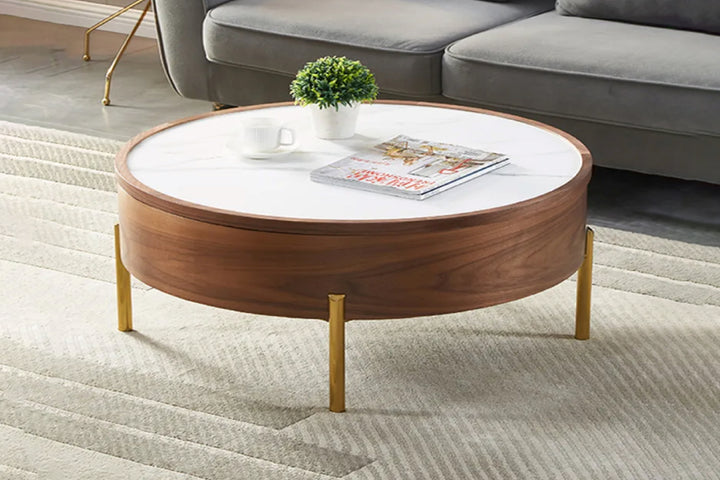 A round coffee table with a white ceramic tabletop, walnut wooden body, and gold stainless steel legs, placed on a grey carpet.