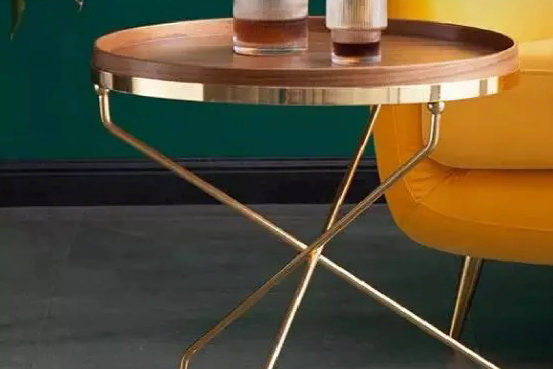 Round wooden table with gold legs next to a yellow chair against a green wall.
