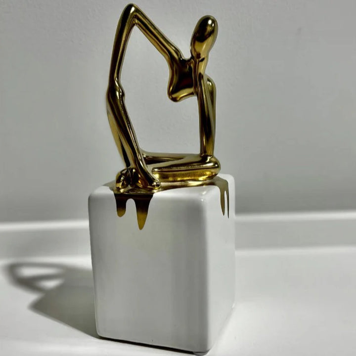 Gold abstract sculpture on a white cube base against a gray background