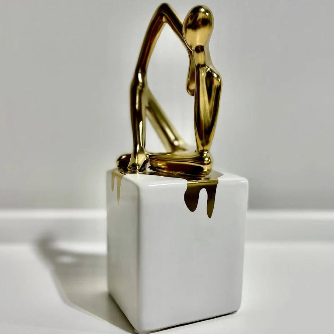Gold sculpture on a white rectangular base against a gray background