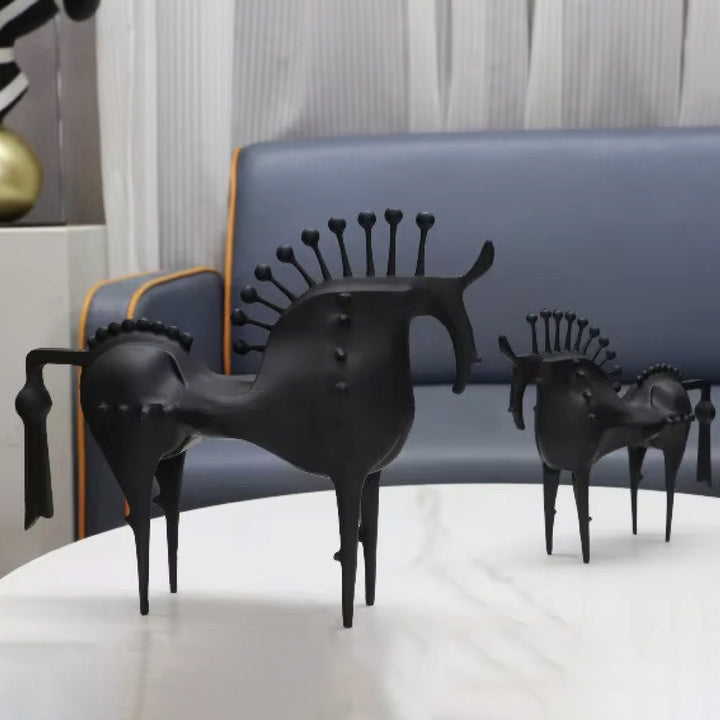 Black horse sculptures on a white surface with a blue sofa in the background