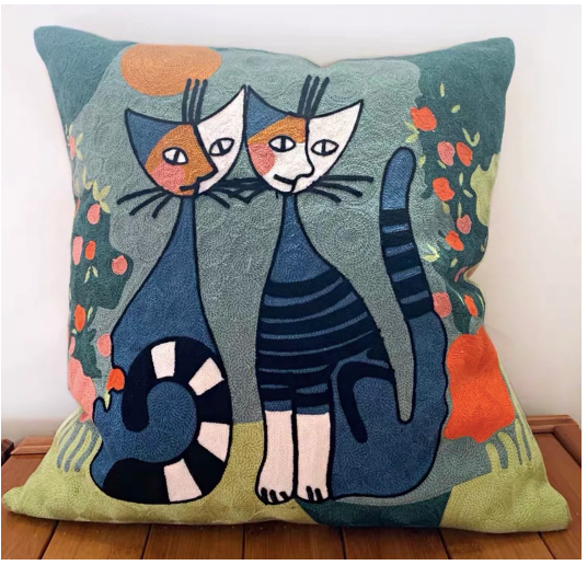 A square-shaped cushion with a colorful design featuring two stylized cats and abstract elements in a garden setting.
