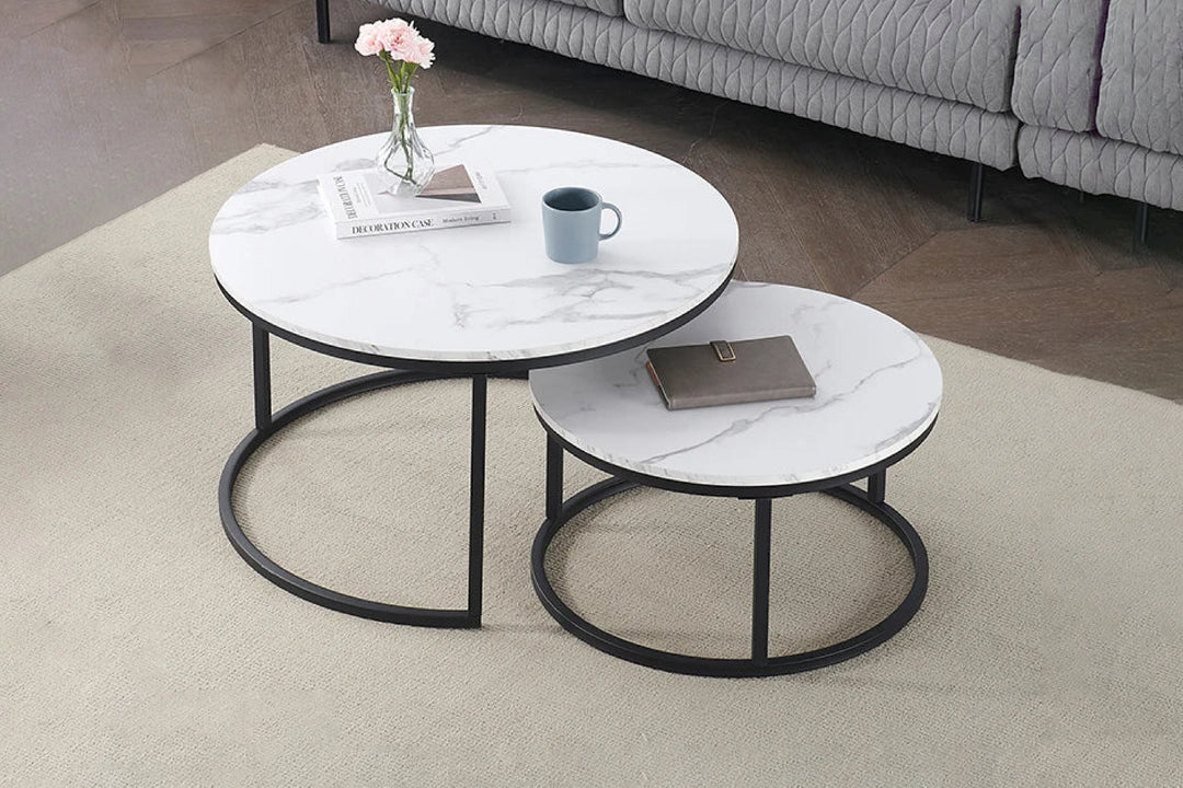 Two nesting coffee tables with a white sintered stone top and black metal base, one larger than the other, placed on a beige carpet.